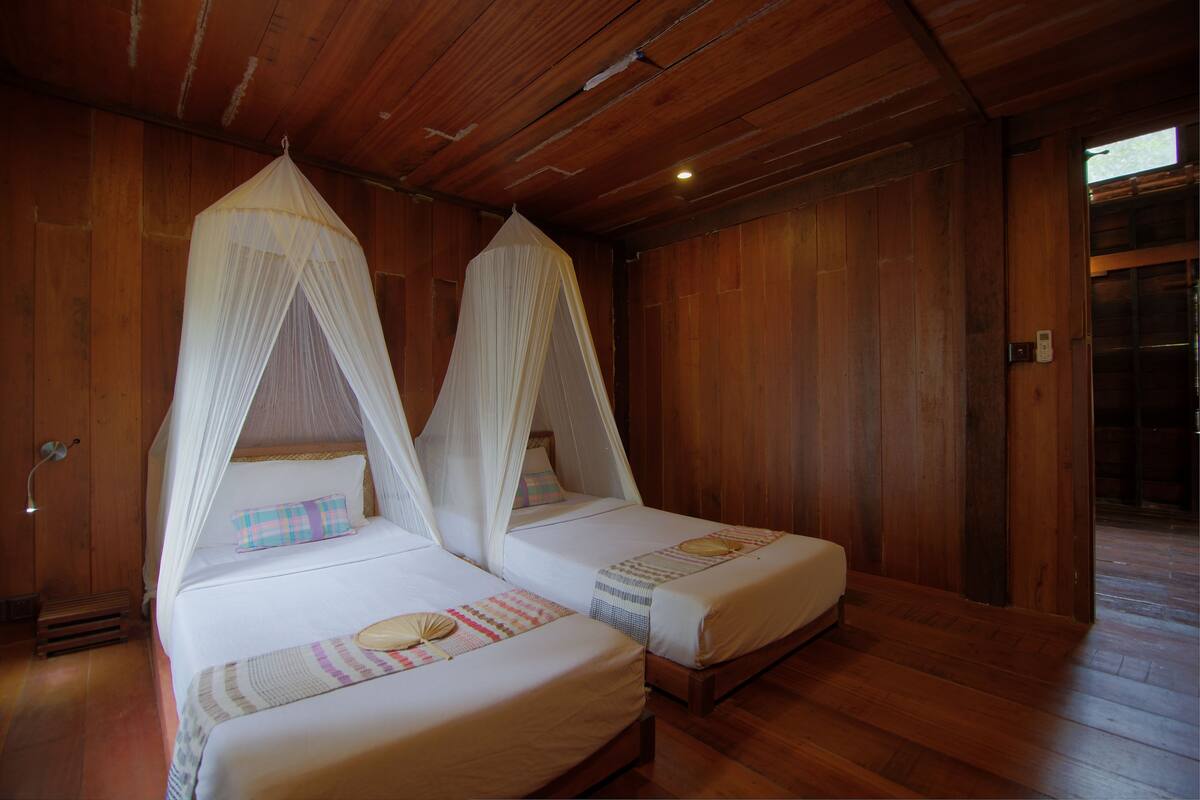 A room with two beds, each with a canopy, wooden walls, and a wooden floor.