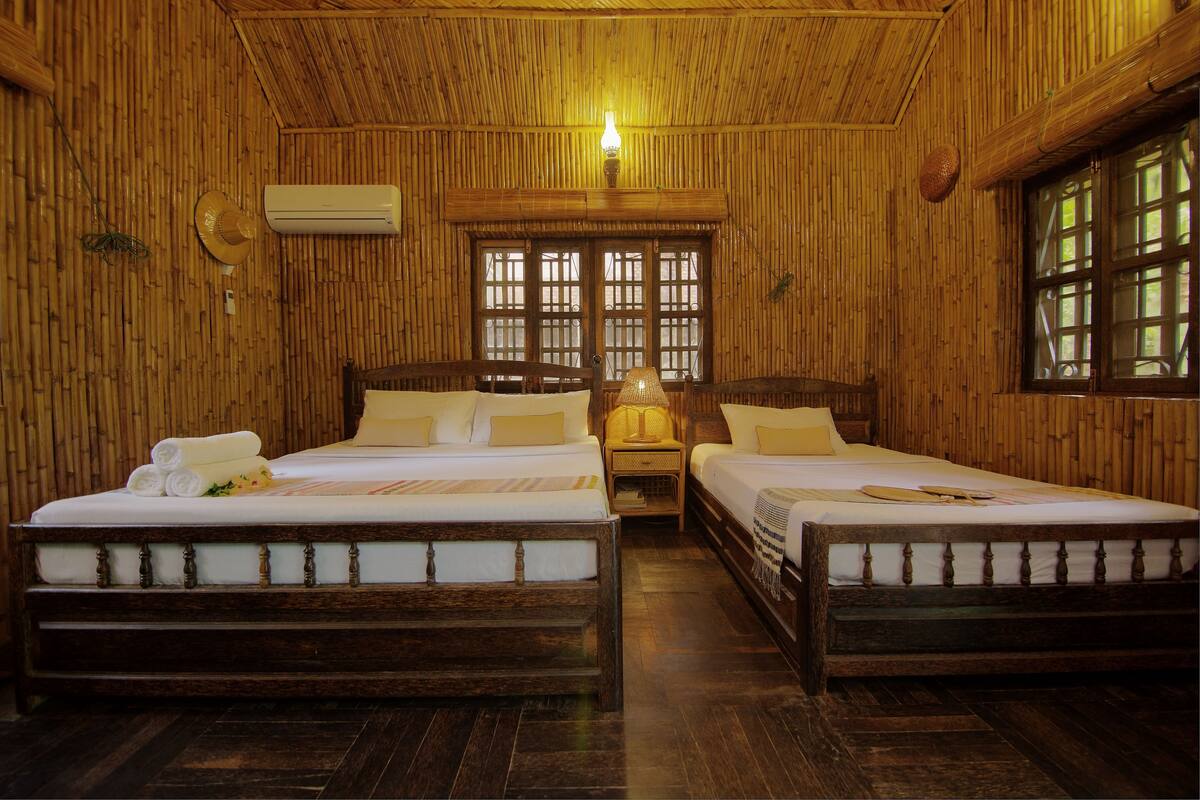 A room with two wooden beds, a nightstand, a lamp, and a window with a view.