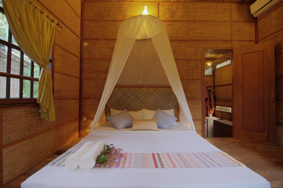 A room with a bed under a canopy, a window with curtains, and a wooden wall.