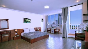 Ein Hotelzimmer mit einem großen Bett, einem Schreibtisch, einem Stuhl, einem kleinen Tisch und einem Balkon mit Blick auf die Stadt.