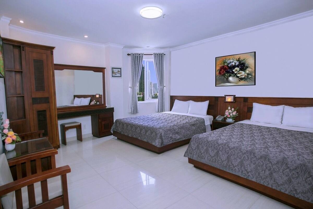 A hotel room with two beds, a desk, a chair, a mirror, and a window with curtains.