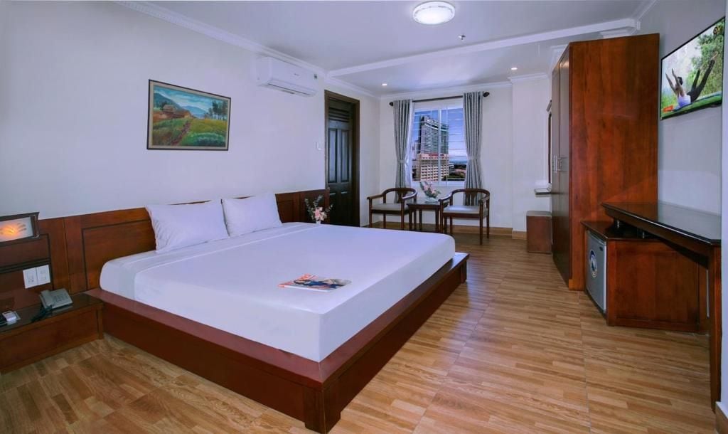 Ein Hotelzimmer mit einem großen Bett, einem Schreibtisch, einem Sessel, einem Fernseher und einem Fenster mit Blick auf Gebäude.