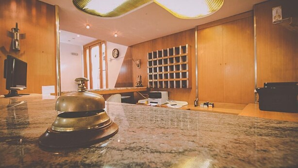 Un vestíbulo de hotel con un mostrador de recepción de mármol, paneles de madera, un reloj y una estantería empotrada con documentos.