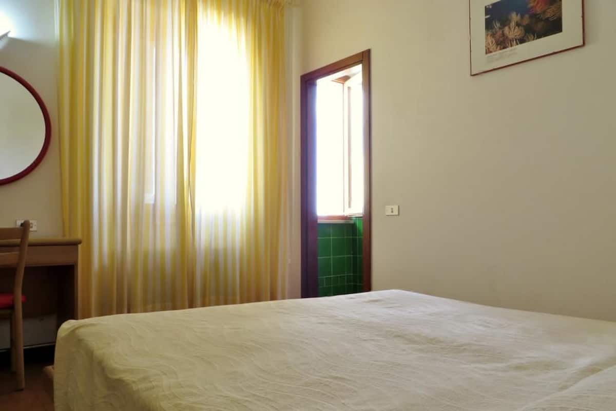 Un dormitorio con cama, una silla, un escritorio y una puerta que da a un baño.
