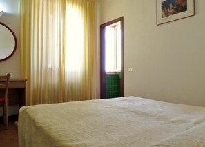 A bedroom with a bed, a chair, a desk, and a door leading to a bathroom. - Hotel Villa Marina (La Maddalena)