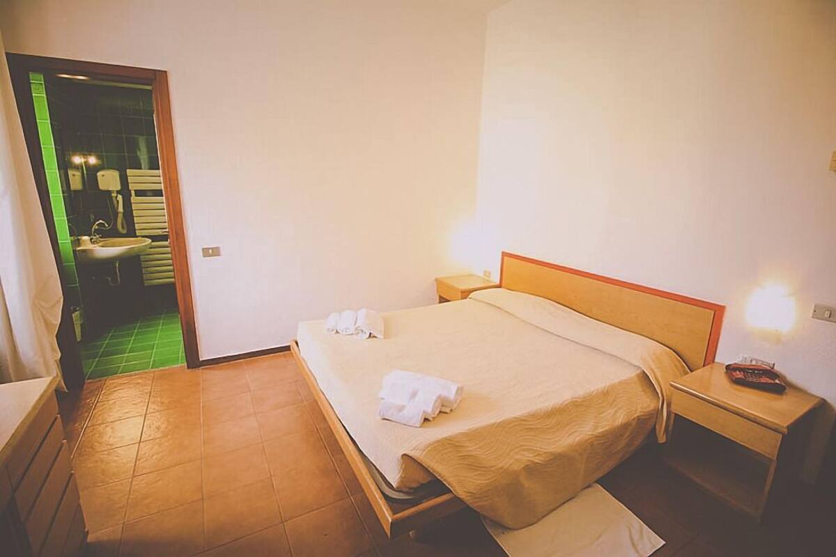 Una habitación de hotel con una cama, una mesita de noche y otra mesita auxiliar.