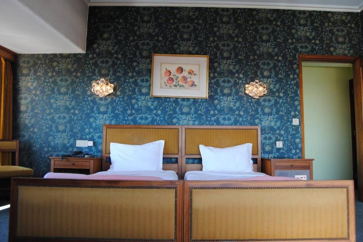 A double bed with a wooden headboard and two nightstands, a framed floral artwork above the bed, and a patterned wallpaper.