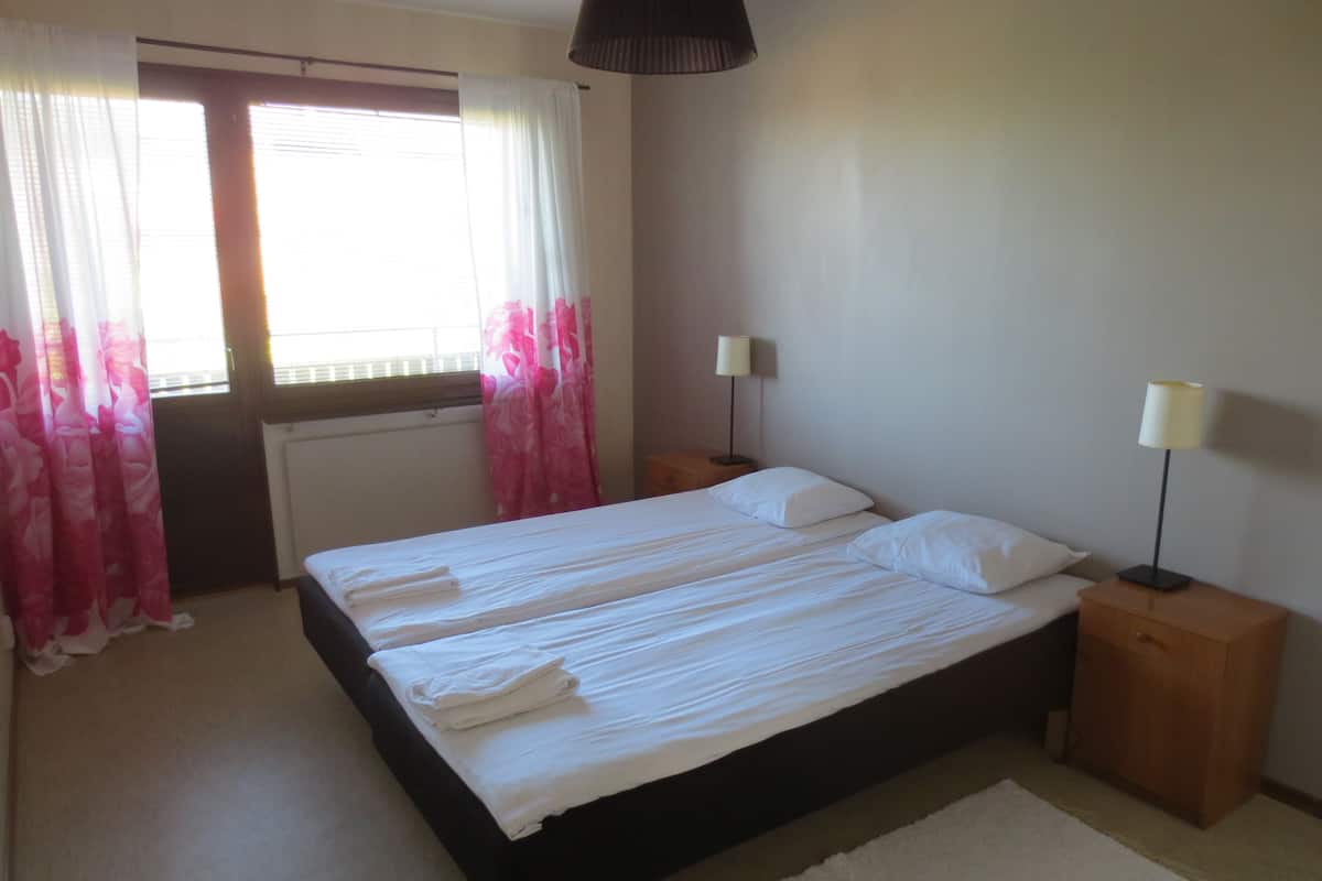 Ein Schlafzimmer mit einem Bett, zwei Nachttischen, einem Fenster mit Vorhängen und einer Lampe auf jedem Tisch.