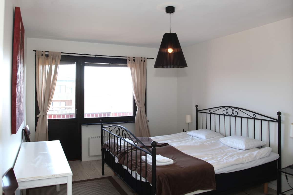 Ein Schlafzimmer mit einem Einzelbett, einem Tisch, einer Hängeleuchte und einem Fenster mit Vorhängen.