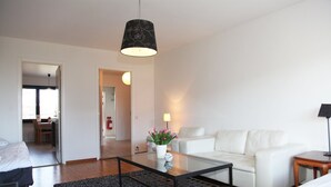Una sala de estar moderna con una mesa de centro de vidrio, sofá blanco y una lámpara negra. Hay una planta en maceta sobre la mesa y un espejo en la pared.