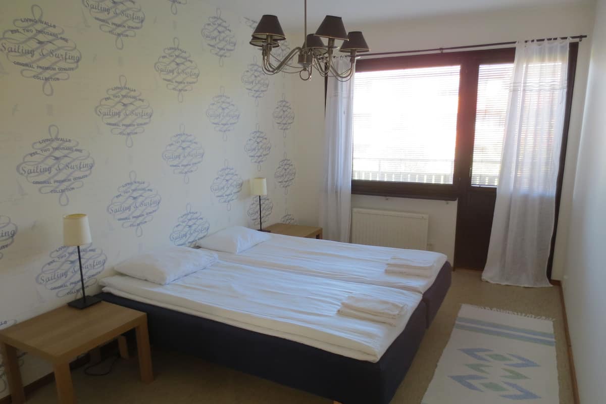 Ein Schlafzimmer mit einem Bett, Nachttischlampen, einem Fenster mit Vorhängen und einer Wand mit Muster.