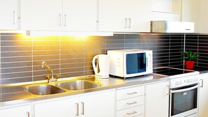 Una cocina moderna con armarios blancos, un lavamanos de acero inoxidable, un microondas, un hervidor y una estufa.
