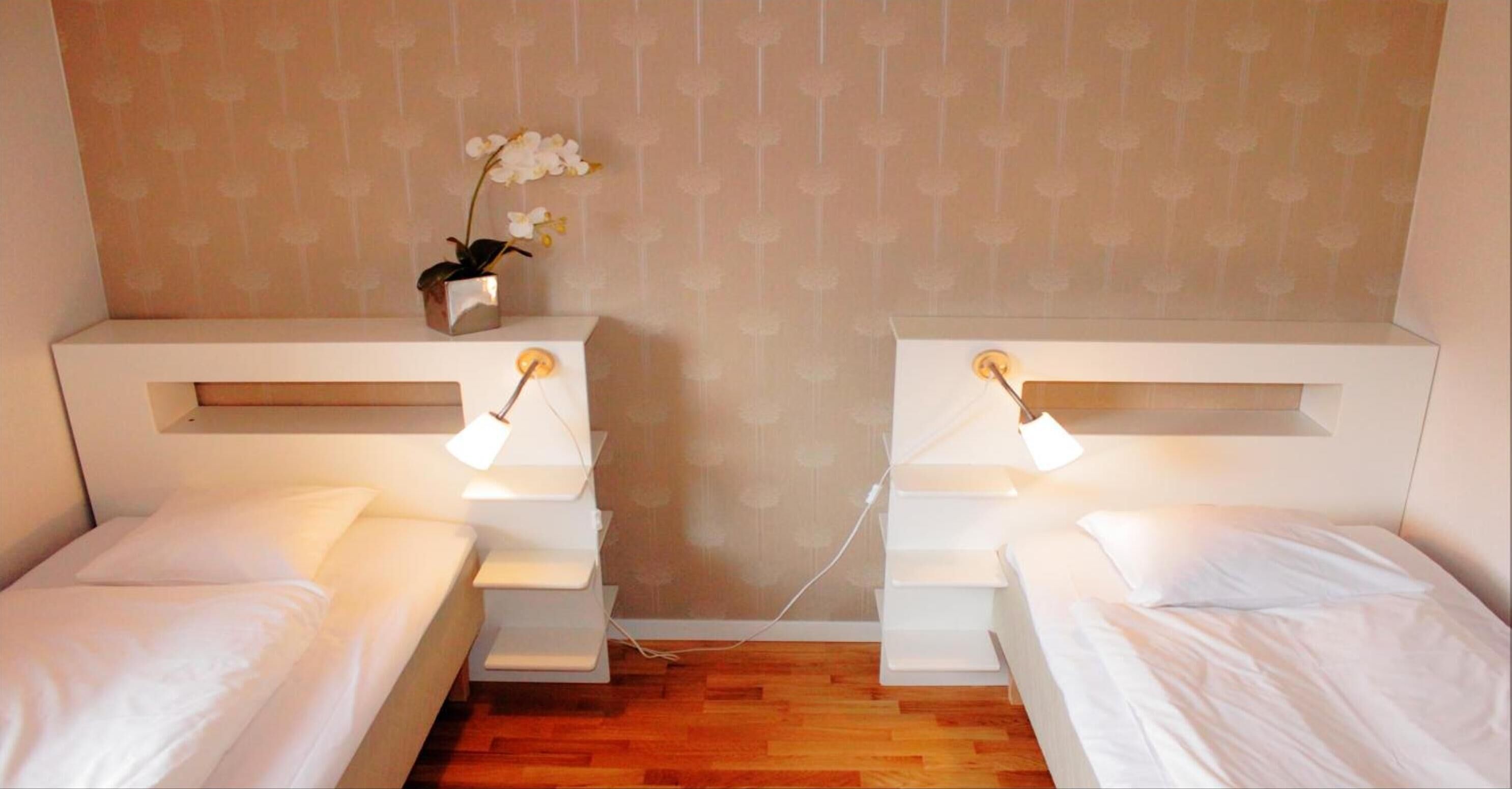 Habitación de hotel con dos camas individuales, una mesita con una orquídea en maceta y una lámpara de pared.