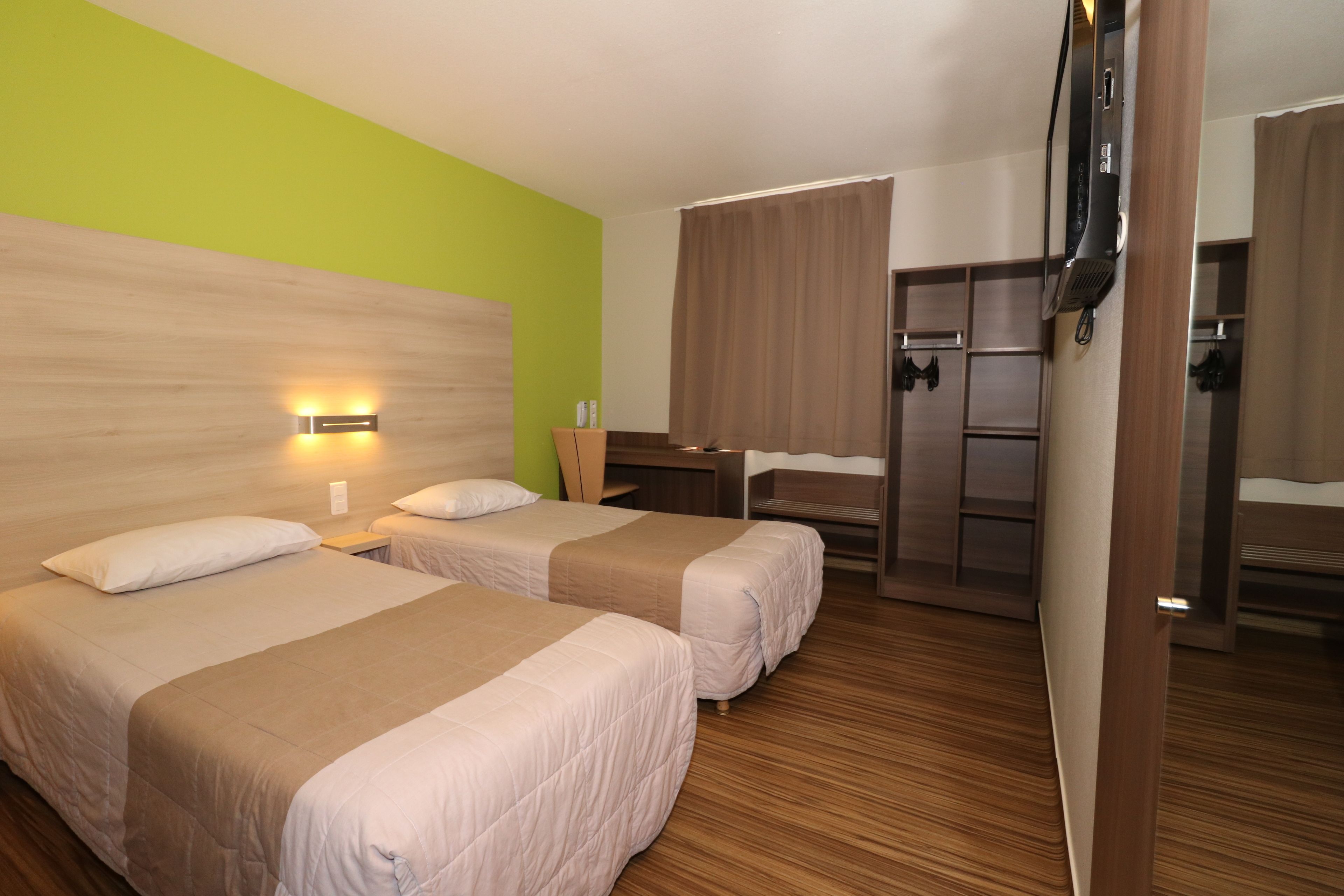 Habitación de hotel con dos camas, un escritorio, un armario y un espejo.