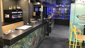 A bar area with a counter, shelves of bottles, and a seating area with stools. - Ekho Hotel Grenoble Nord Saint Egrève (Saint-Egreve)