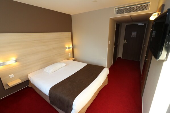 Habitación de hotel con cama, alfombra roja, cabecera de madera y televisión montada en la pared.