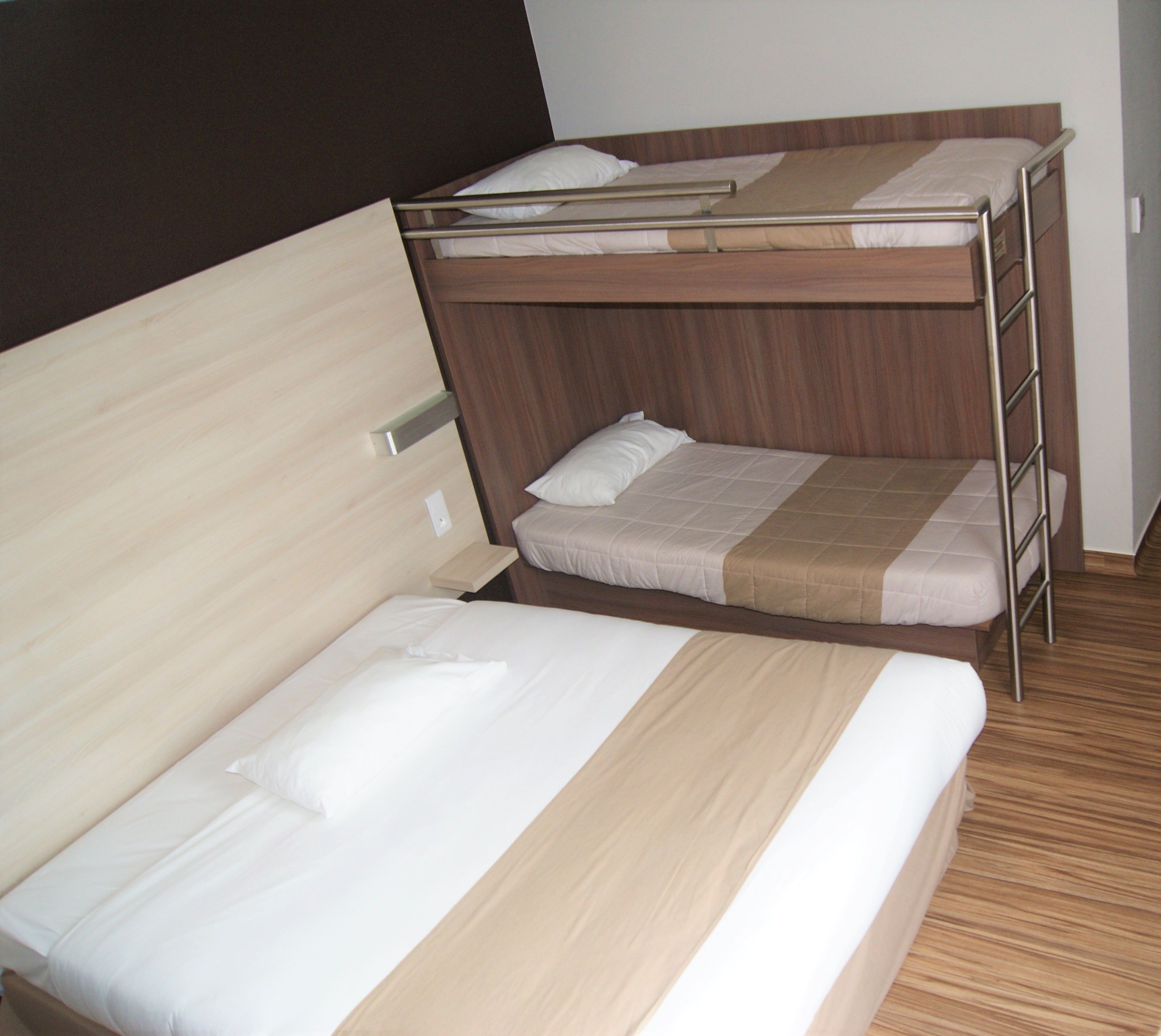 Een stapelbed met een onderbed en een enkel bed, beide met houten frames en witte beddengoed.