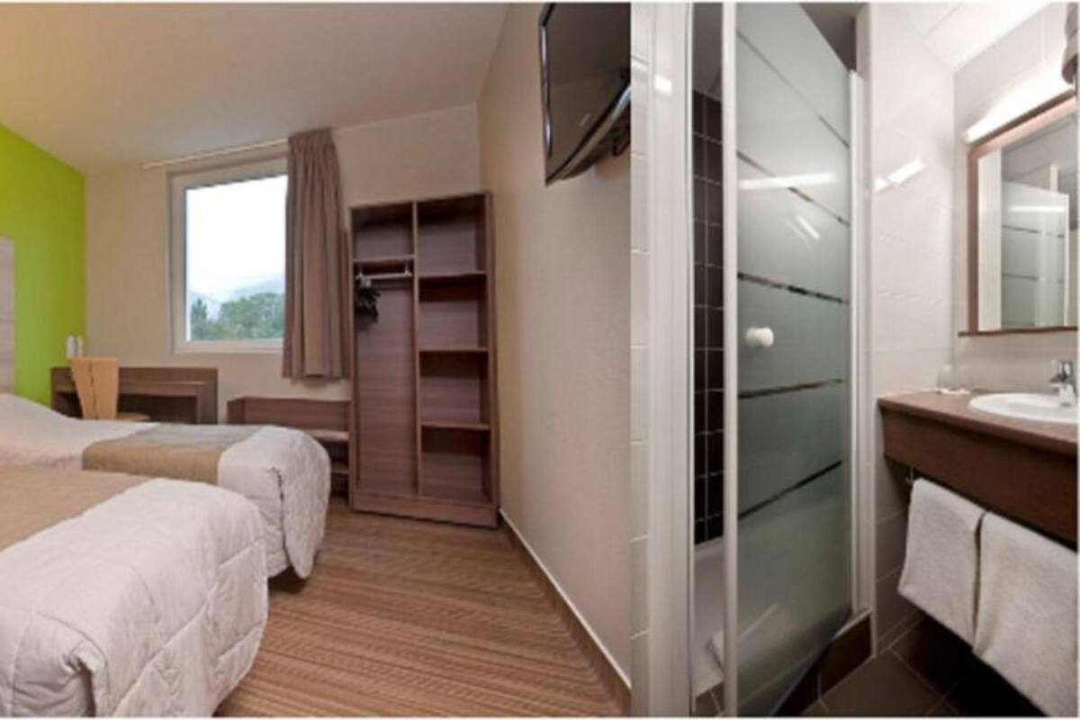 Une chambre d’hôtel avec deux lits, un grand placard, une salle de bain avec un miroir et une télévision.