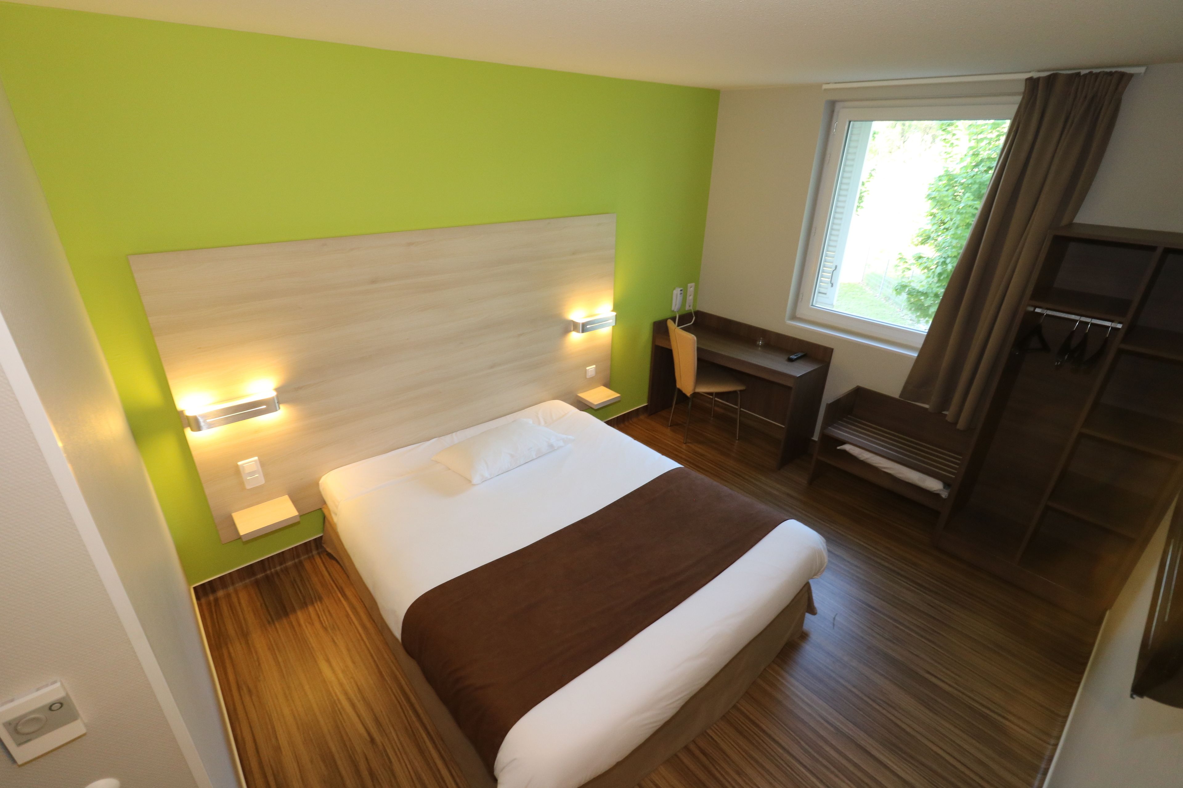 Une chambre d’hôtel moderne avec un grand lit, un bureau et une fenêtre avec des rideaux.