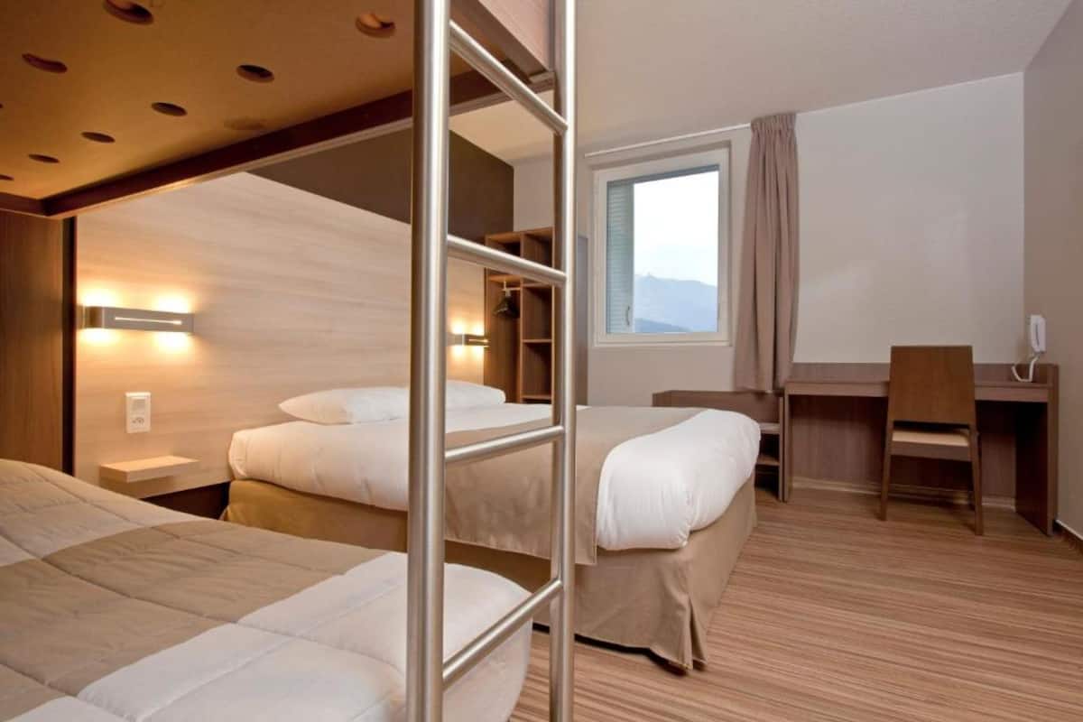 Une chambre d’hôtel avec des lits superposés, un bureau et une fenêtre donnant sur un paysage agréable.