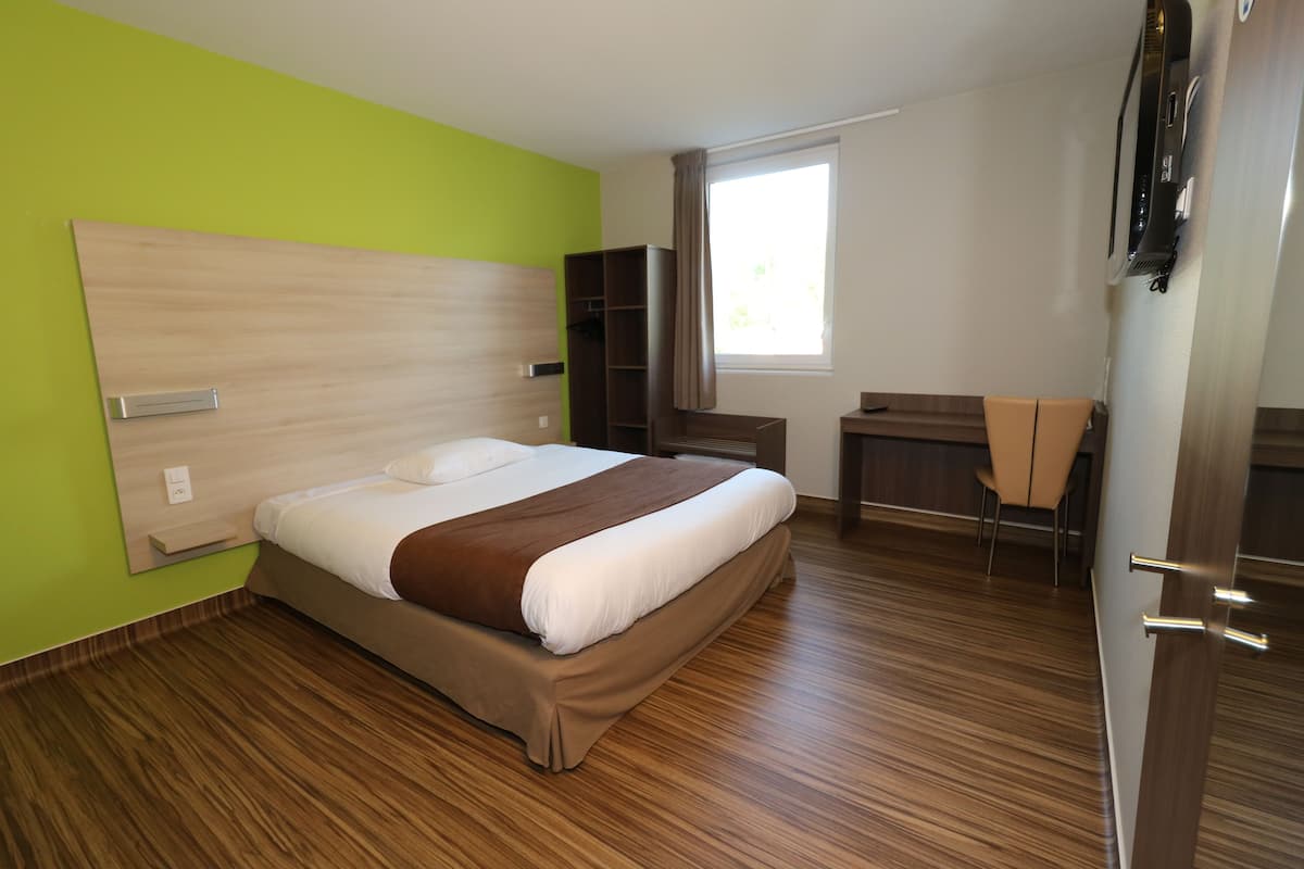 Une chambre d’hôtel moderne dotée d’un grand lit, d’un bureau, d’une armoire et d’une fenêtre laissant entrer la lumière naturelle.
