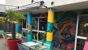 An outdoor seating area with colorful tables and chairs, a large potted plant, and a vibrant mural on the wall. - Ekho Hotel Grenoble Nord Saint Egrève (Saint-Egreve)