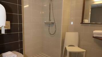 Une salle de bain avec des toilettes, une douche et une chaise.