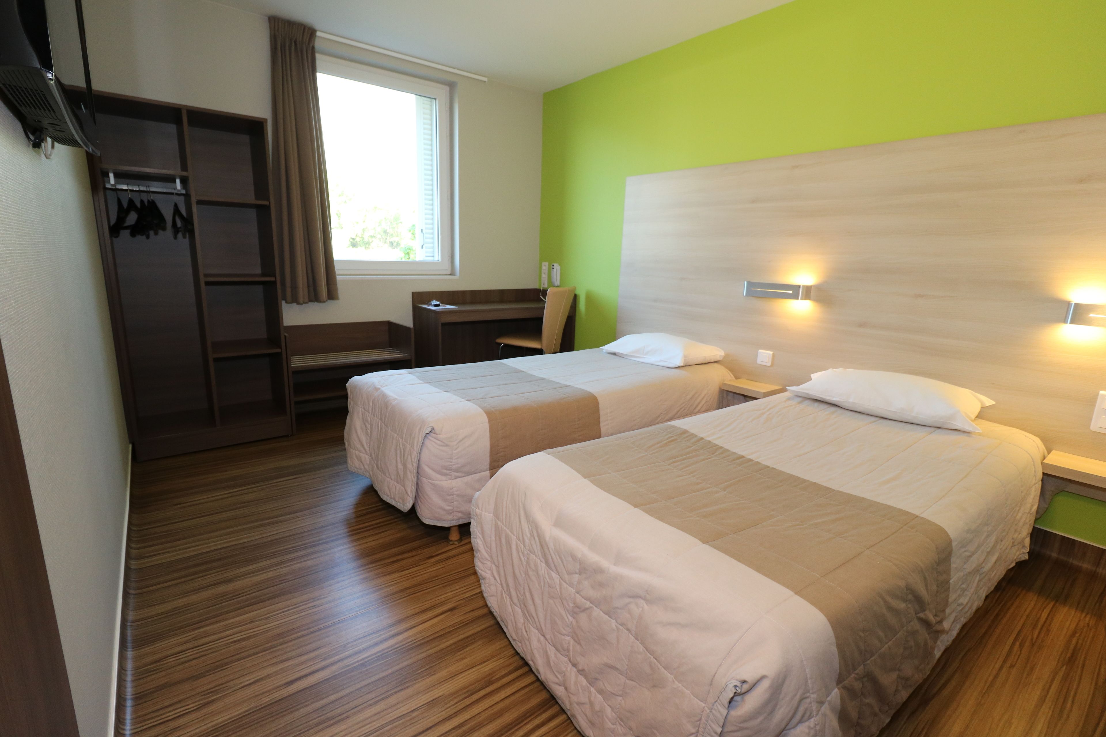 Een hotelkamer met twee bedden, een bureau, een stoel, een kledingkast en een raam met gordijnen.