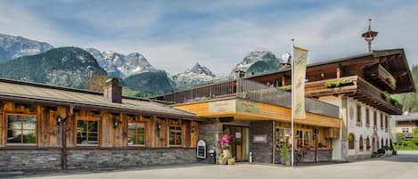 A traditional wooden building with a balcony, stone facade, and mountain views.