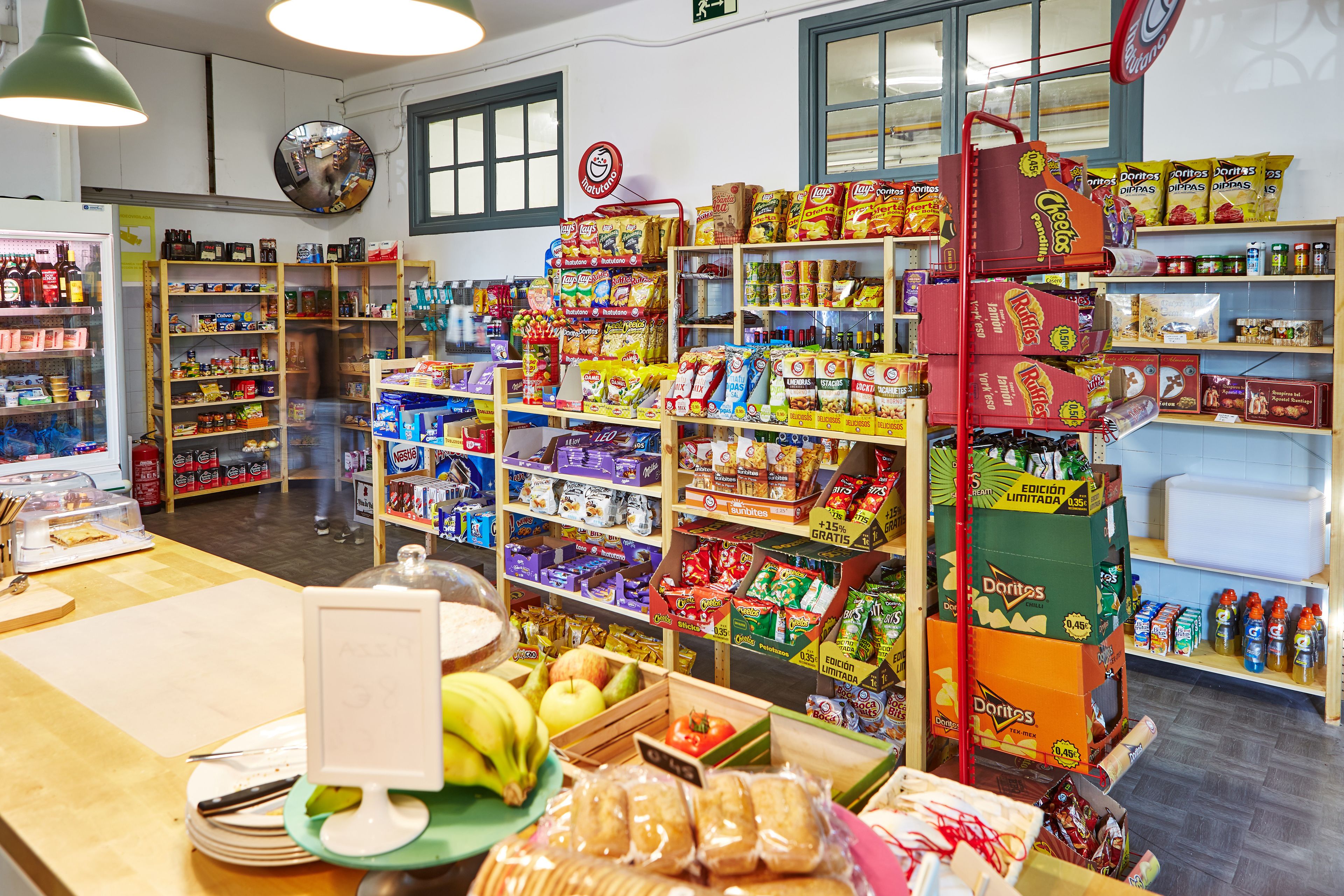Interieur van een supermarkt met schappen vol snacks, een etalage met vers fruit en een gekoeld gedeelte.