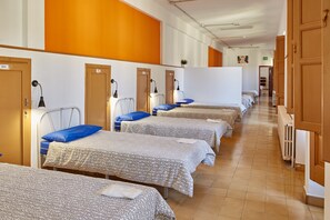 A corridor with multiple beds arranged in rows, each with a headboard and a bedside lamp. - Albergue Seminario Menor - Hostel (Santiago de Compostela)