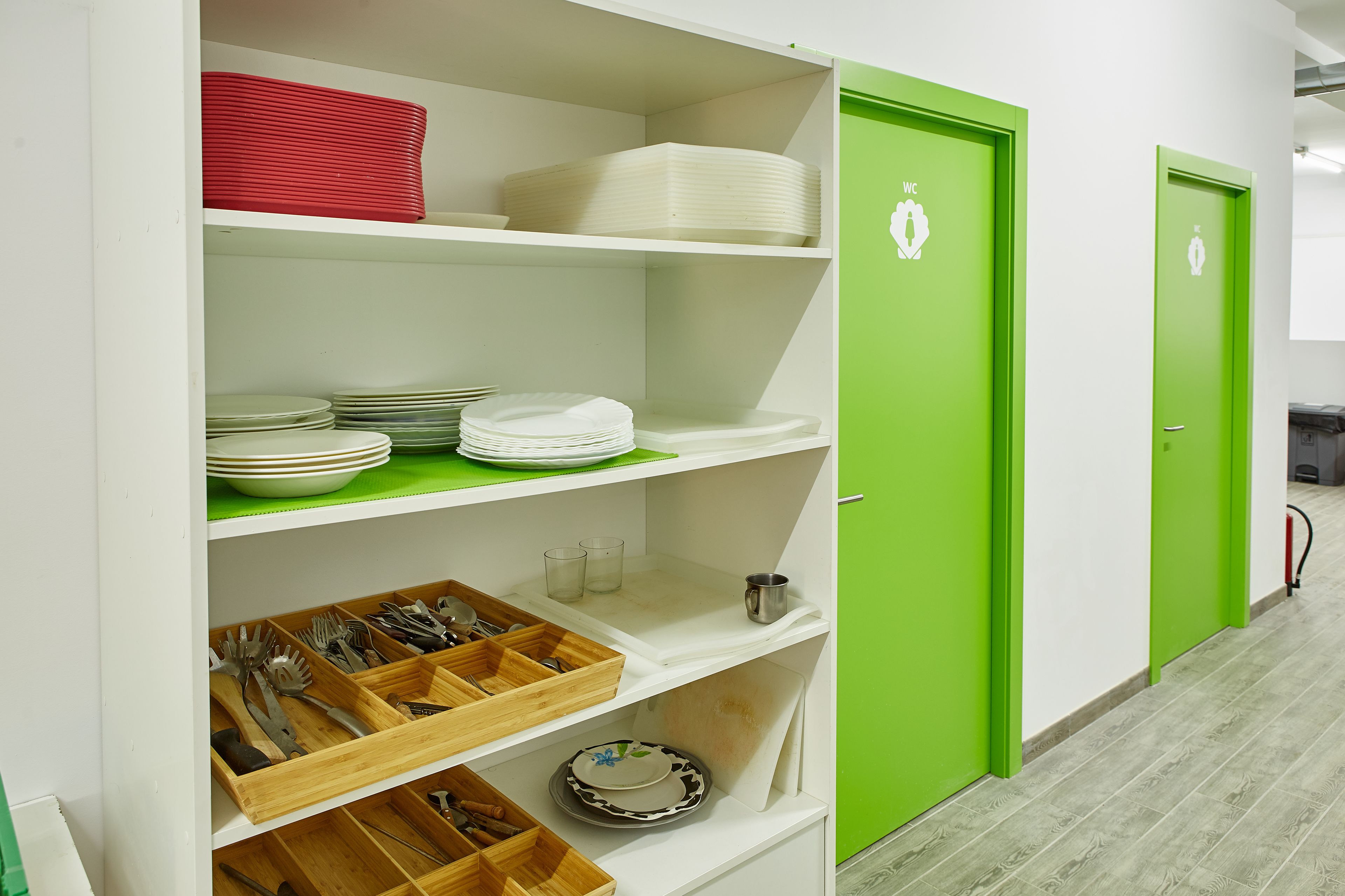 Una cocina con estantes blancos y puertas verdes, que contiene platos, tazones y utensilios.