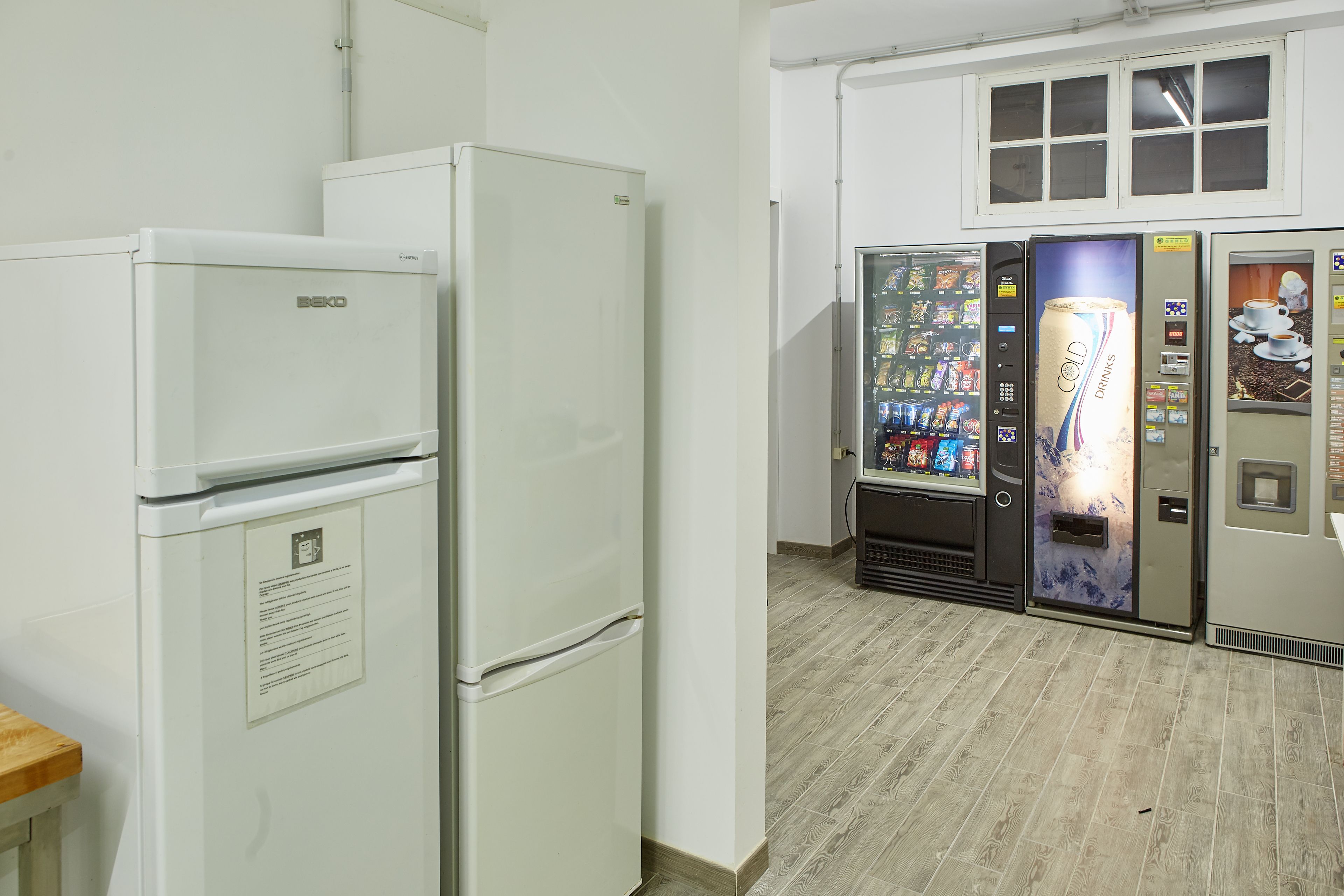 A kitchenette with a refrigerator, a microwave, and a vending machine with drinks.