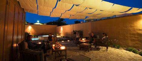An outdoor patio area with tables and chairs under a canopy, surrounded by walls and a pool.