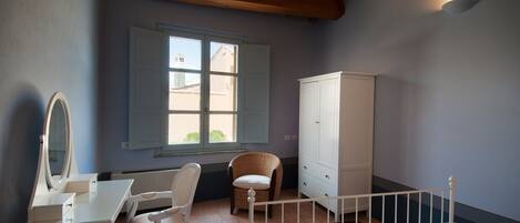 Une chambre à coucher comprenant un lit, une commode, une chaise, un bureau avec un miroir et une fenêtre avec des volets.