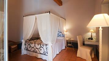 A bedroom with a four-poster bed, a bedside table with a lamp, a chair, and a small table with a telephone.