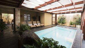 Un área de piscina con terraza de madera, sillones de descanso y plantas en macetas.