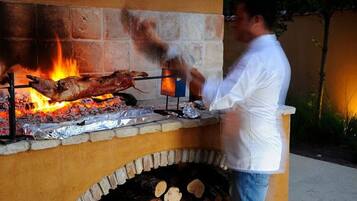 Une personne est en train de cuire un cochon entier sur un barbecue extérieur, avec un four en briques et un feu allumé en dessous.