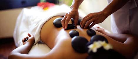A person receiving a hot stone massage with multiple stones placed on their back.