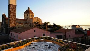 Un edificio histórico con una torre y una cúpula destacadas, rodeado de viviendas y un patio ajardinado.