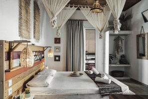 A bedroom with a wooden headboard, a large bed, a woven hanging light fixture, and a view of a balcony with a plant. - Kanela Studios (Zakynthos)