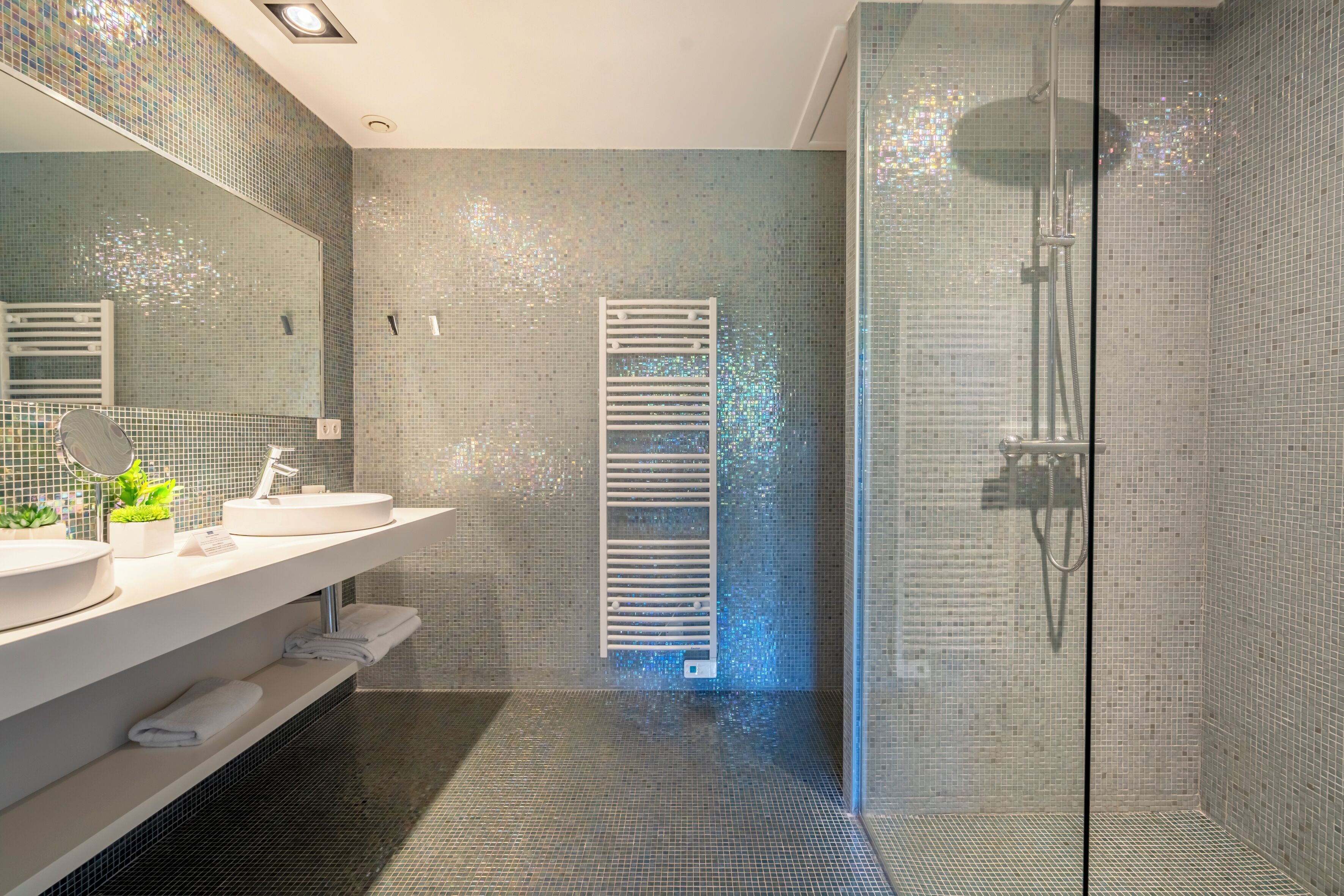 Ein modernes Badezimmer mit einer gläsernen Duschkabine, einem weißen Waschbecken und einem Spiegel darüber.