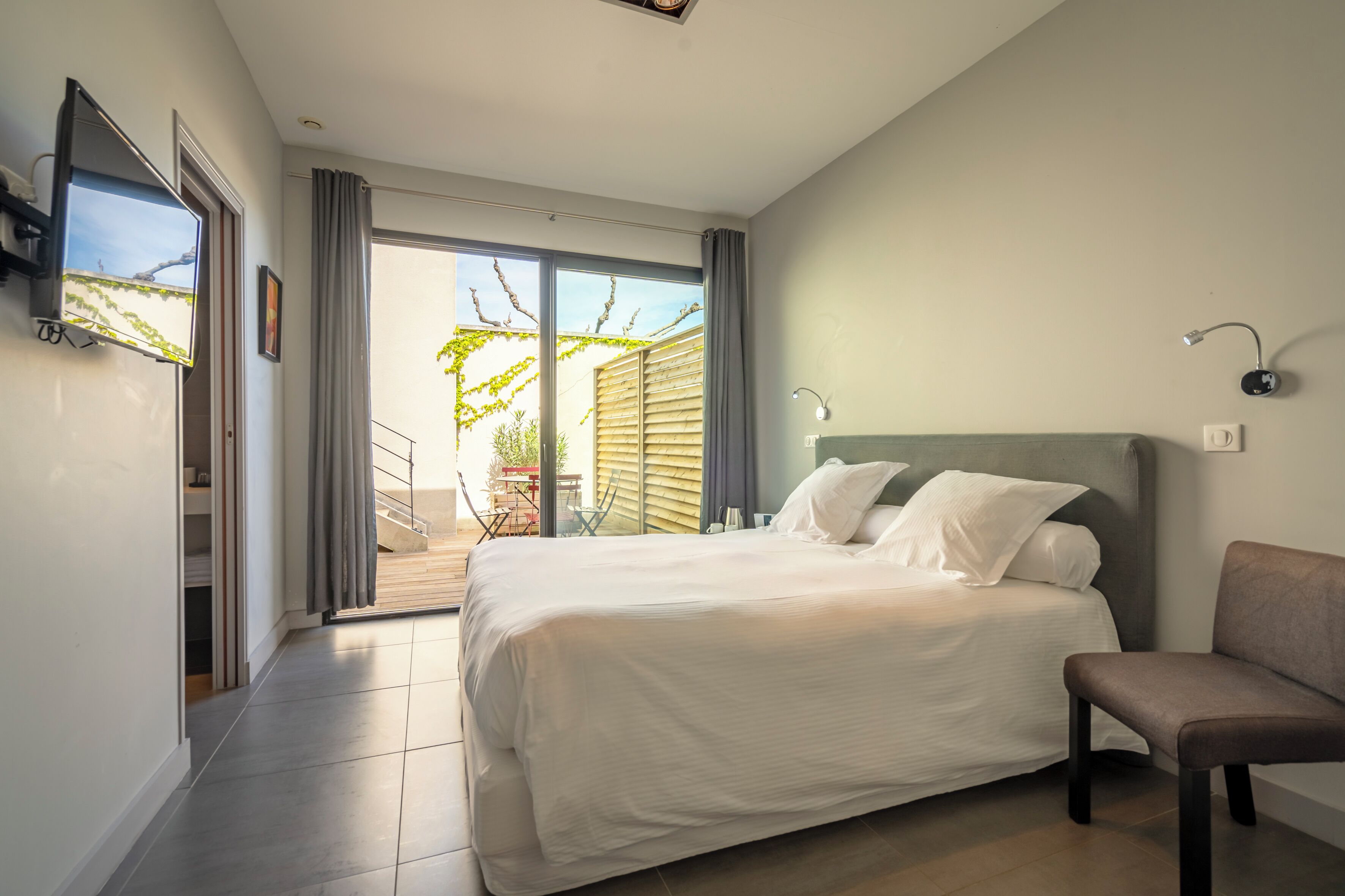 Un dormitorio con cama, una silla, un televisor y un puerta corrediza de vidrio que da a un balcón.