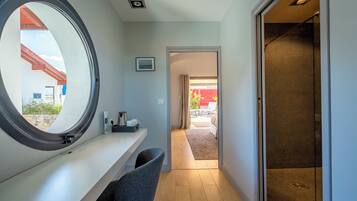 A hallway with a round window, a small desk with a chair, and a shower area with a glass door.