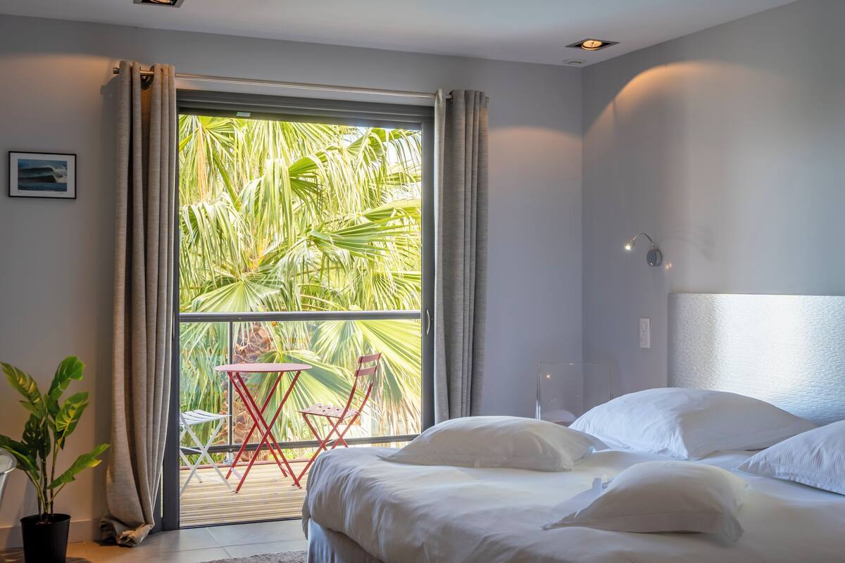 A bedroom with a large window, a bed, a small table, and chairs.