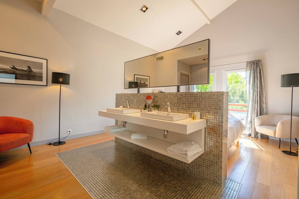 A modern bathroom with a large mirror, two sinks, and a red chair.