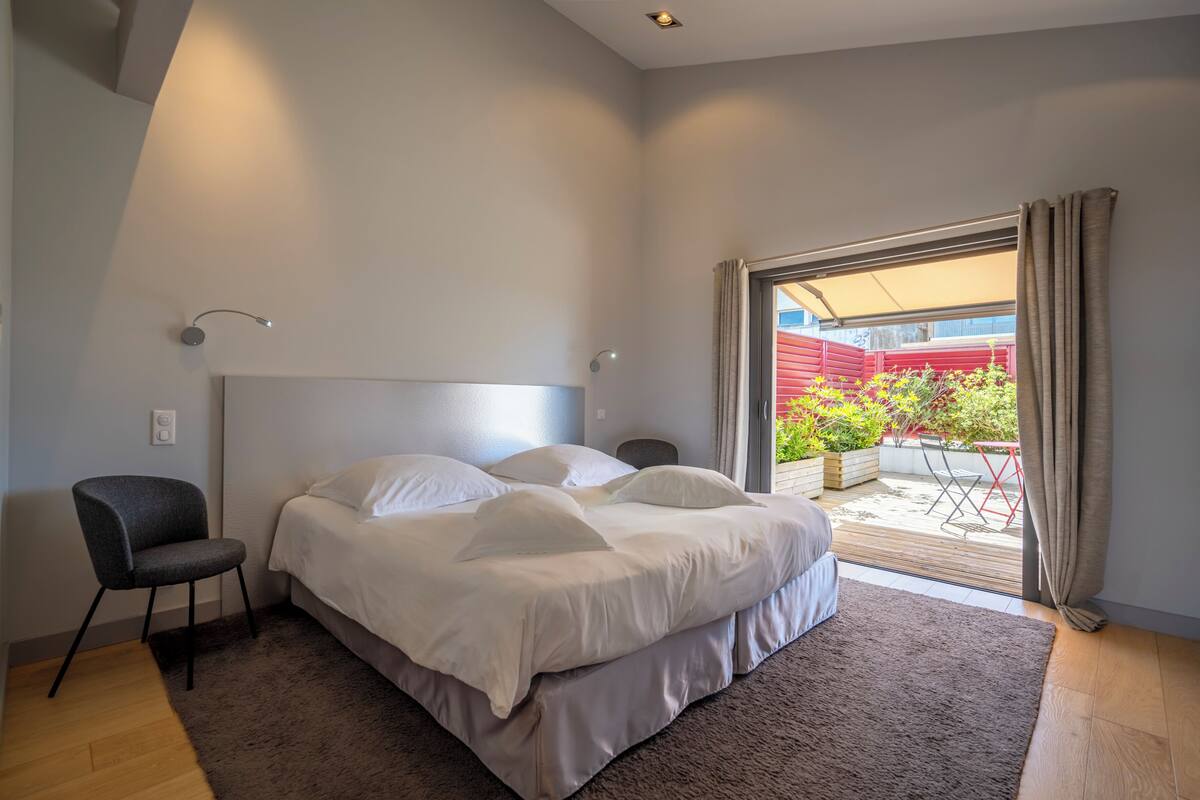 A modern bedroom with a large bed, a chair, and a view of the outside.