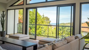 A modern living room with a large sliding glass door leading to a balcony with a view of greenery and the sea. - Lafitenia Resort (Saint-Jean-de-Luz)