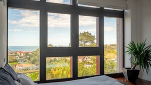A bedroom with a large window offering a view of a coastal town and the sea. - Lafitenia Resort (Saint-Jean-de-Luz)