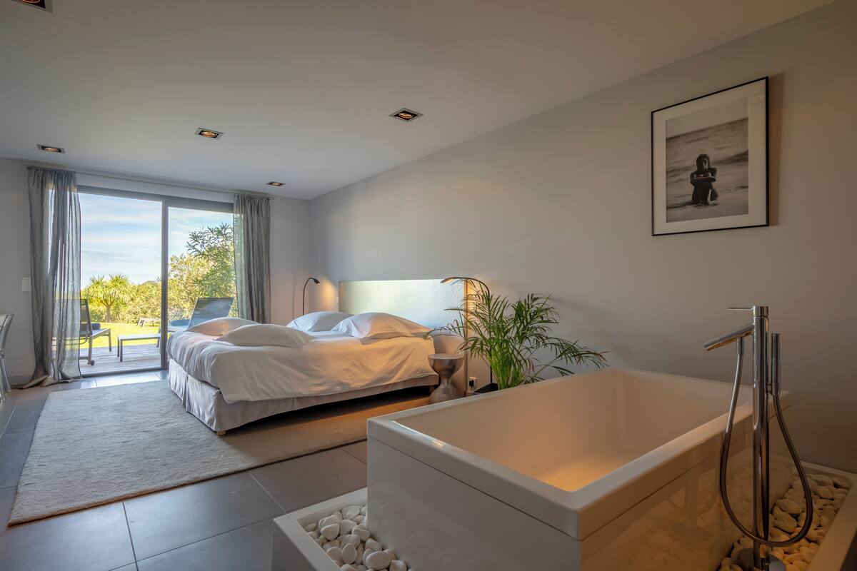 A modern bedroom with a large bed, a bathtub, and a view of the outdoors.